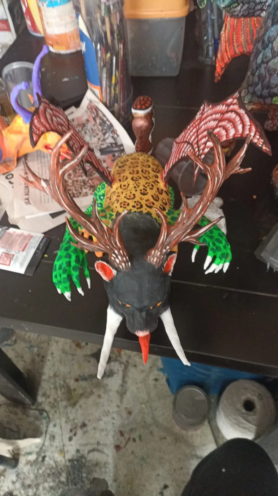 Overhead view of the alebrije in the workshop: red wings spread and spotted body.