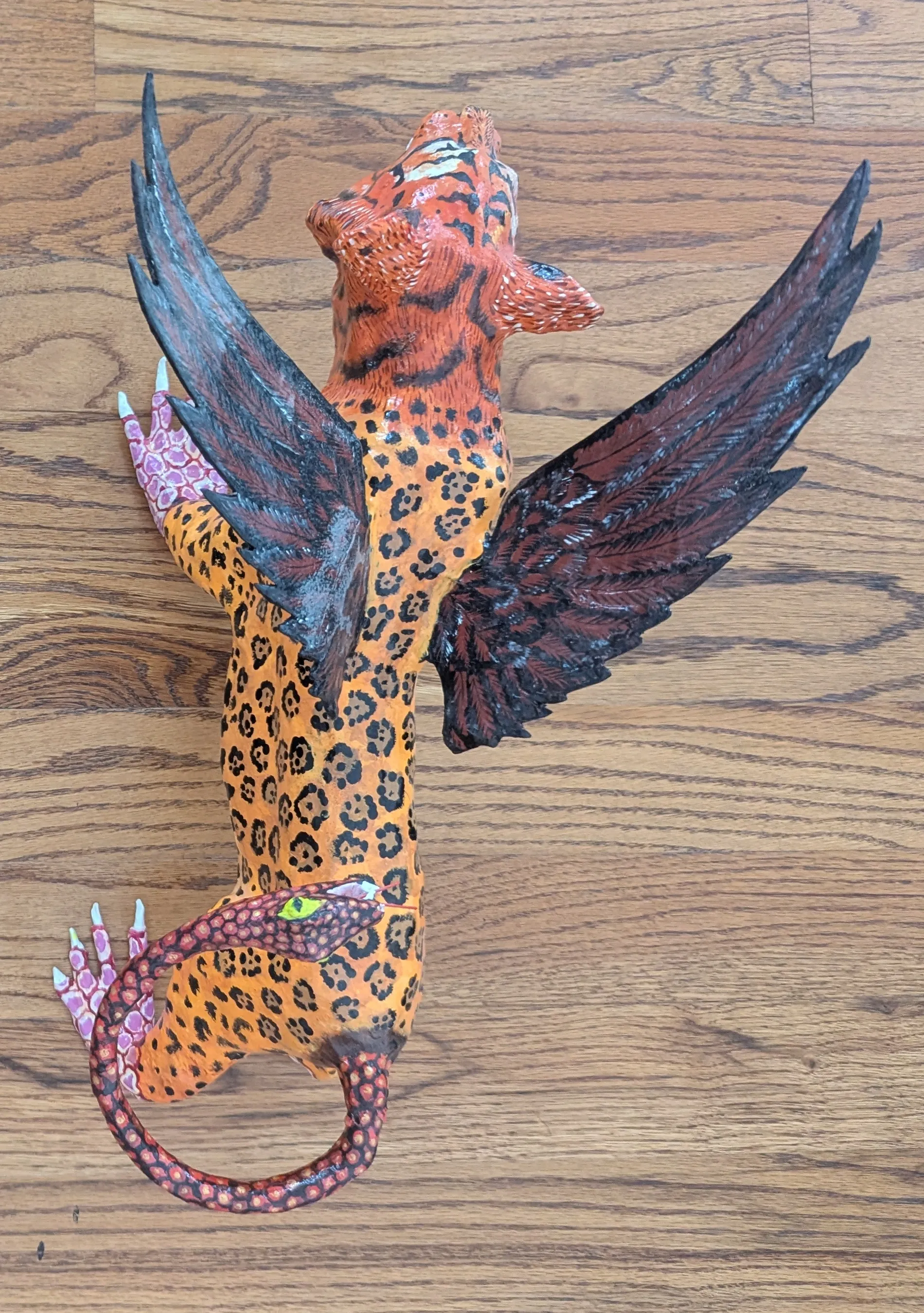 Vista cenital del alebrije de tigre: las alas negras abiertas y la cola enroscada que termina en cabeza de serpiente.