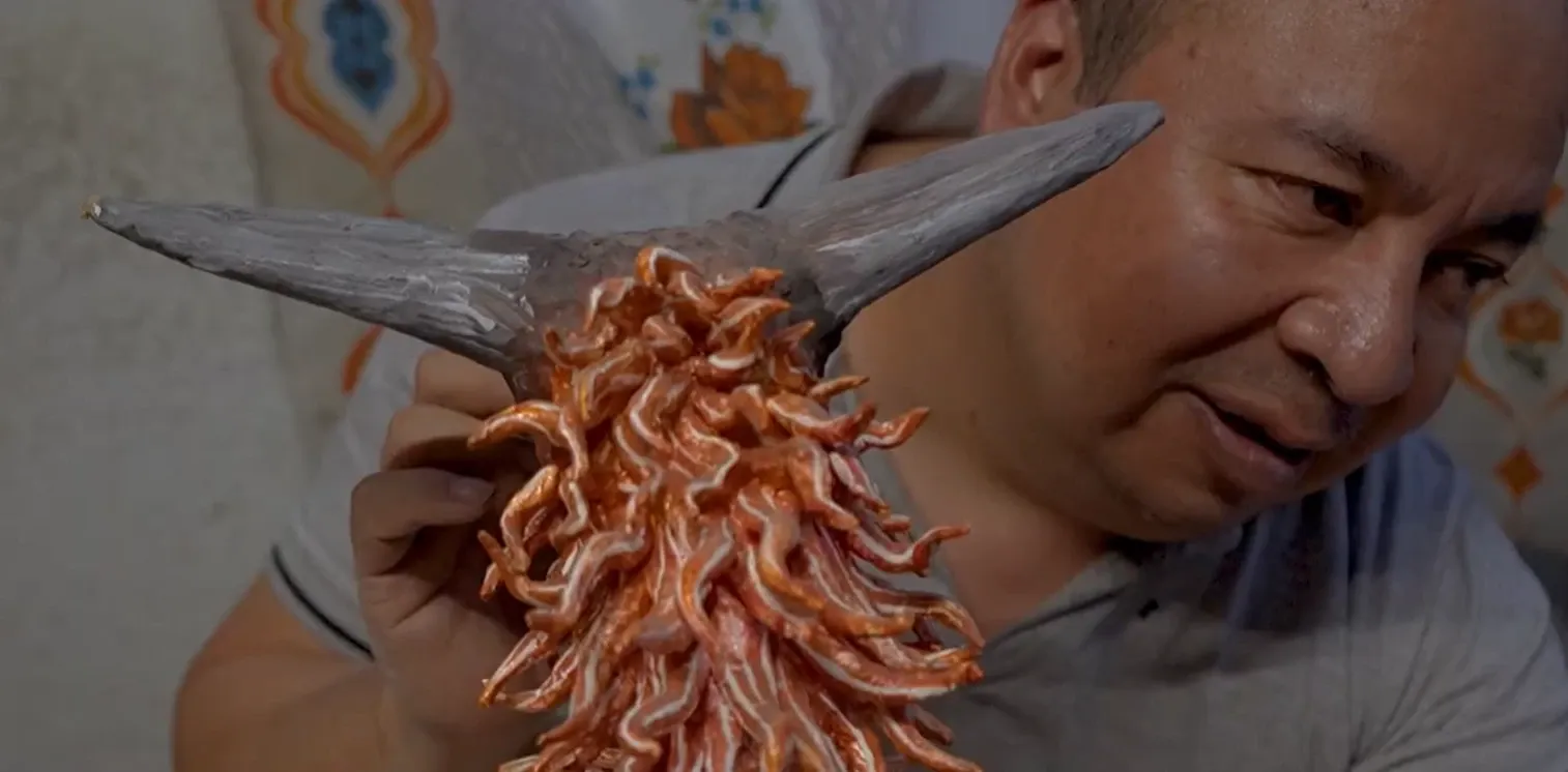 Felipe Linares Vargas looks closely at an alebrije head in progress, with grey horns and a mane of orange strips.