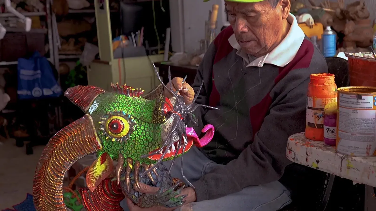 Felipe Linares Mendoza sostiene con las dos manos un alebrije verde de cartonería.