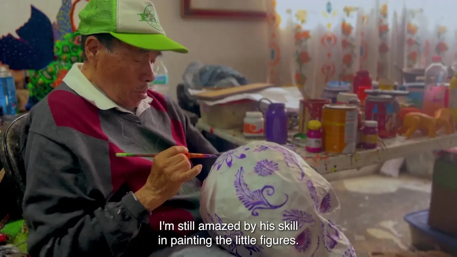Felipe Linares Mendoza, in a green cap, paints a cartonería sphere with a brush.