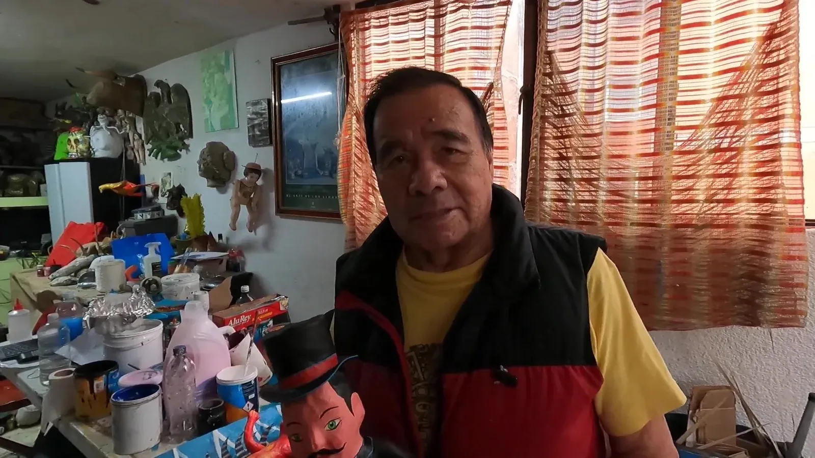 Felipe Linares Mendoza, con chaleco rojo, en su taller; al fondo, alebrijes terminados.