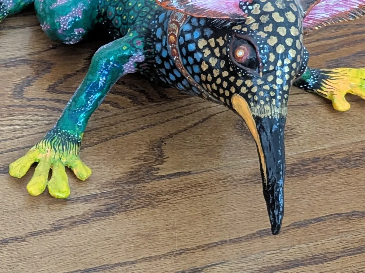 A bird’s head on a frog’s body; the neck scaled in blue and gold.