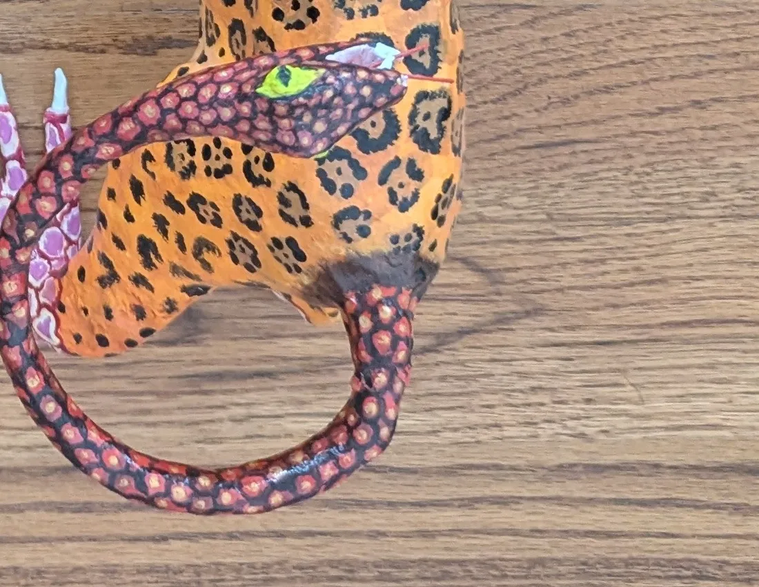 The tiger’s tail ends in a yellow-eyed serpent head.